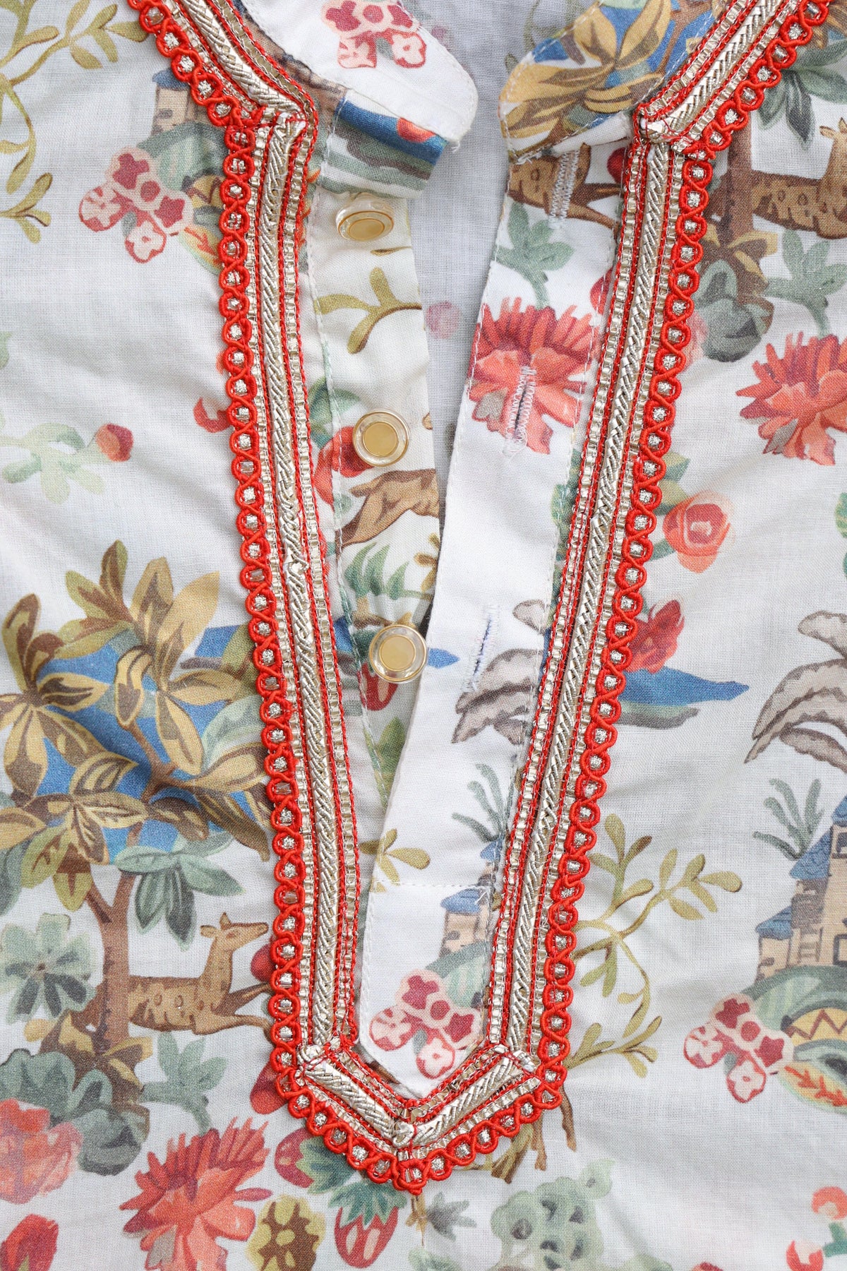 Close-up of a printed kurta or tunic with a white base, featuring a colorful botanical and animal pattern, and a prominent red and gold embroidered V-neckline.
